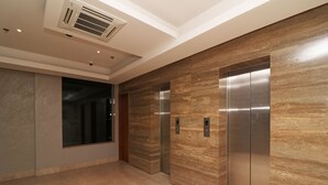 Un área de ascensor moderna con suelo de mármol, un ventanal grande y una pared con textura similar a madera.