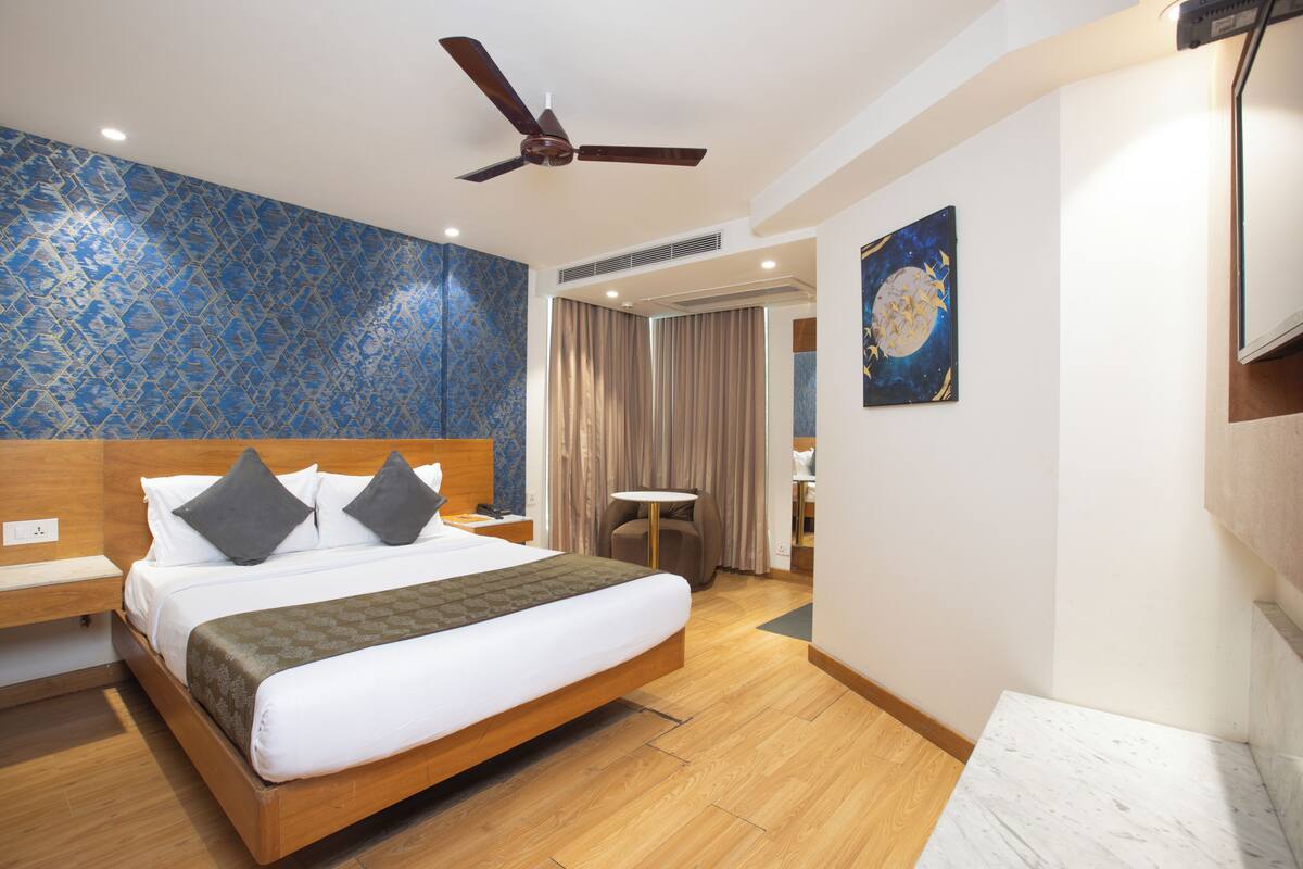 Ein Hotelzimmer mit einem hölzernen Bett, einem Deckenventilator, einer blauen Wand mit Muster, einem Gemälde und einem Holzboden.