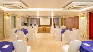 Un salón de conferencias con sillas y mesas blancas, un atril y una pantalla que muestra 