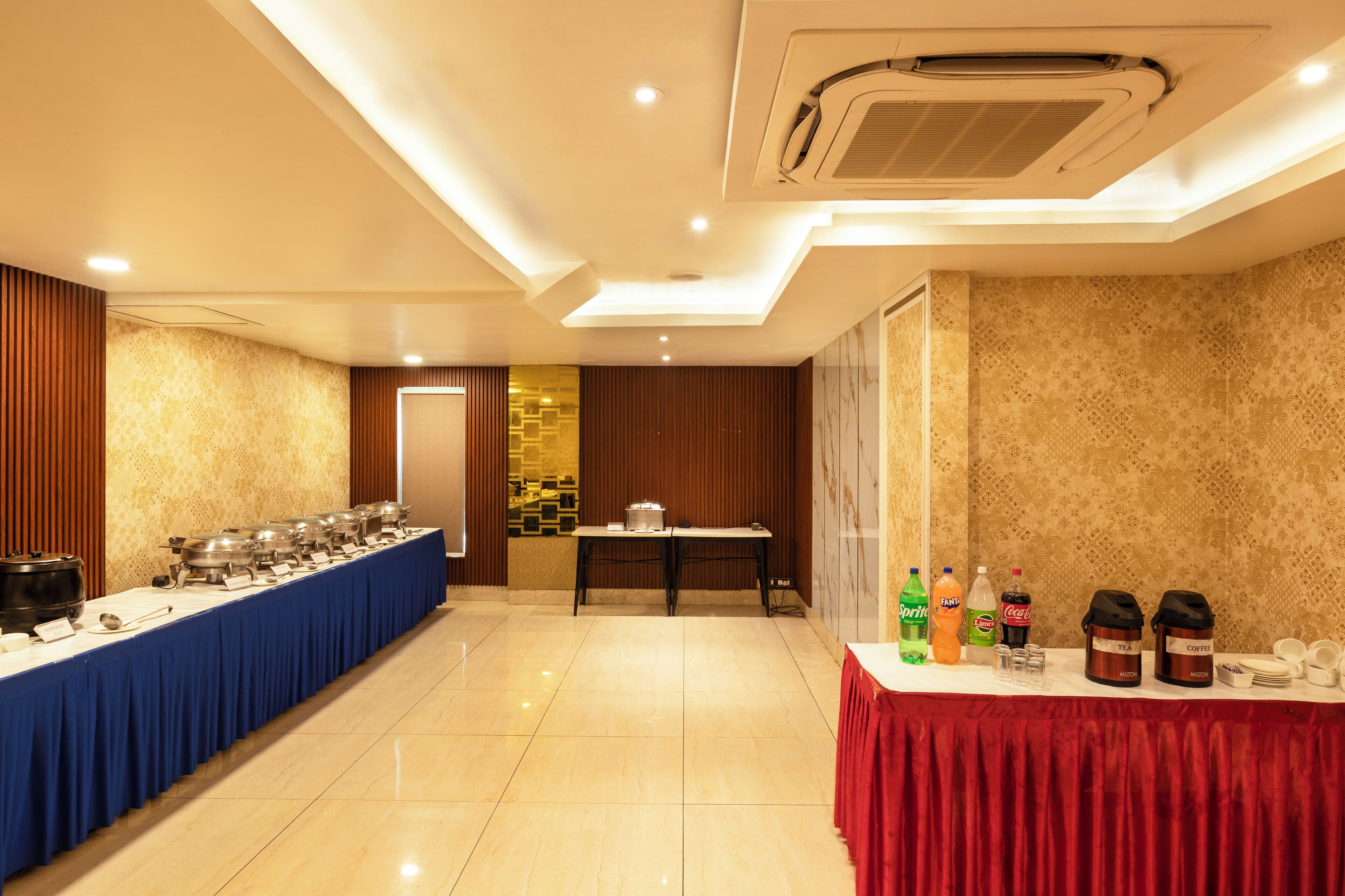 A buffet setup with multiple serving stations, a table with beverages, and a wall with patterned wallpaper.