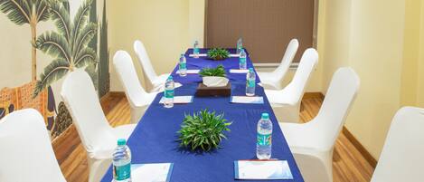 A conference room with a long table, white chairs, water bottles, and a blue tablecloth.