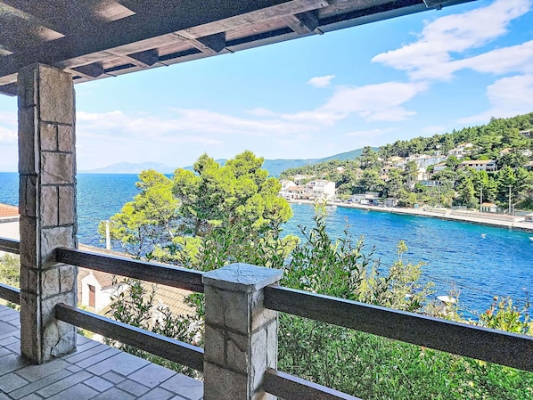 A balcony with a view of a coastal town, stone pillars, and a clear blue sea.