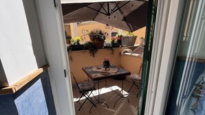 An open sliding glass door leading to a patio with a table and chairs, potted plants, and a hanging light fixture. - "Casetta del Borghetto" - "In the Heart of the Borghetto" Near the sea and Rome. (Nettuno)