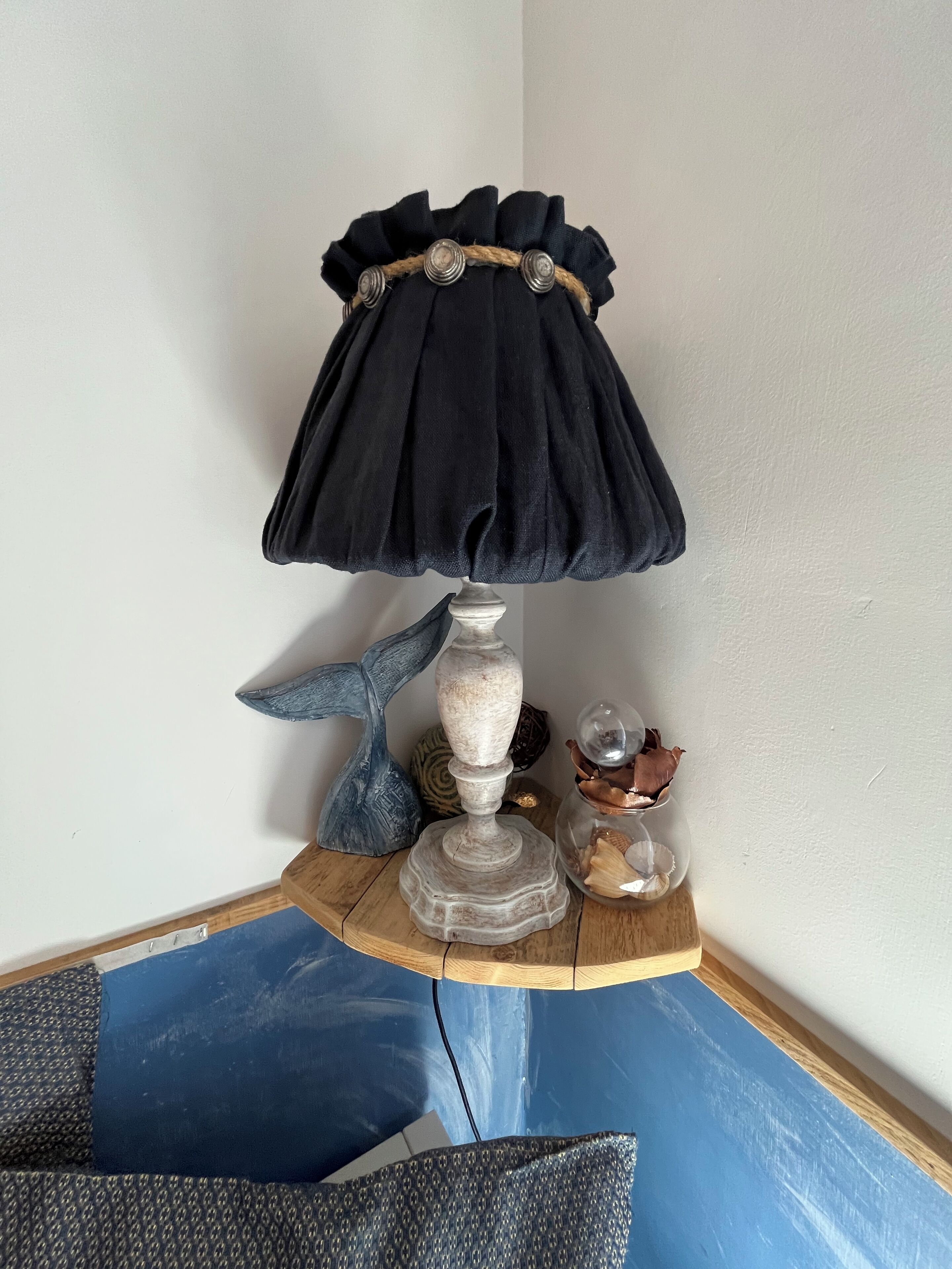 A corner table with a lamp, decorative items, and a blue cushion.