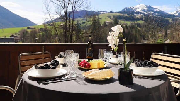 Une table dressée à l’extérieur, avec une vue sur les montagnes, une bouteille de vin et une assiette de nourriture.
