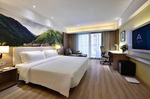 A hotel room with a large bed, a desk, a chair, and a TV.