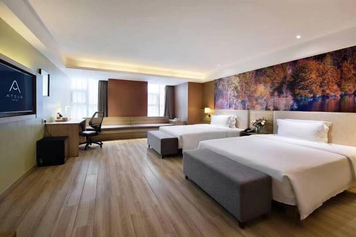 A hotel room with two beds, a desk, a chair, and a large painting on the wall.