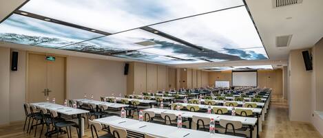 Un salón de conferencias con filas de mesas y sillas, una pantalla de proyección grande y un techo con diseño de árbol y cielo.