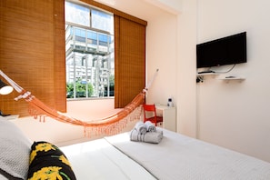 A hotel room with a bed, a desk, a chair, a TV, and a hammock. - Omar do Rio - VP303 (Rio de Janeiro)