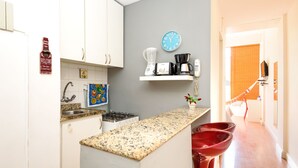 A kitchen with white cabinets, a granite countertop, a coffee maker, a blender, and a clock on the wall. - Omar do Rio - VP303 (Rio de Janeiro)
