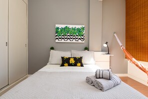 A neatly arranged bedroom with a bed, pillows, a nightstand, a lamp, and a hammock. - Omar do Rio - VP303 (Rio de Janeiro)
