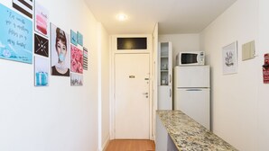 A narrow hallway with a white door, a microwave, and a refrigerator on the right. - Omar do Rio - VP303 (Rio de Janeiro)