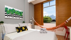 A bedroom with a bed, pillows, a hammock, a desk, and a window with a view. - Omar do Rio - VP303 (Rio de Janeiro)
