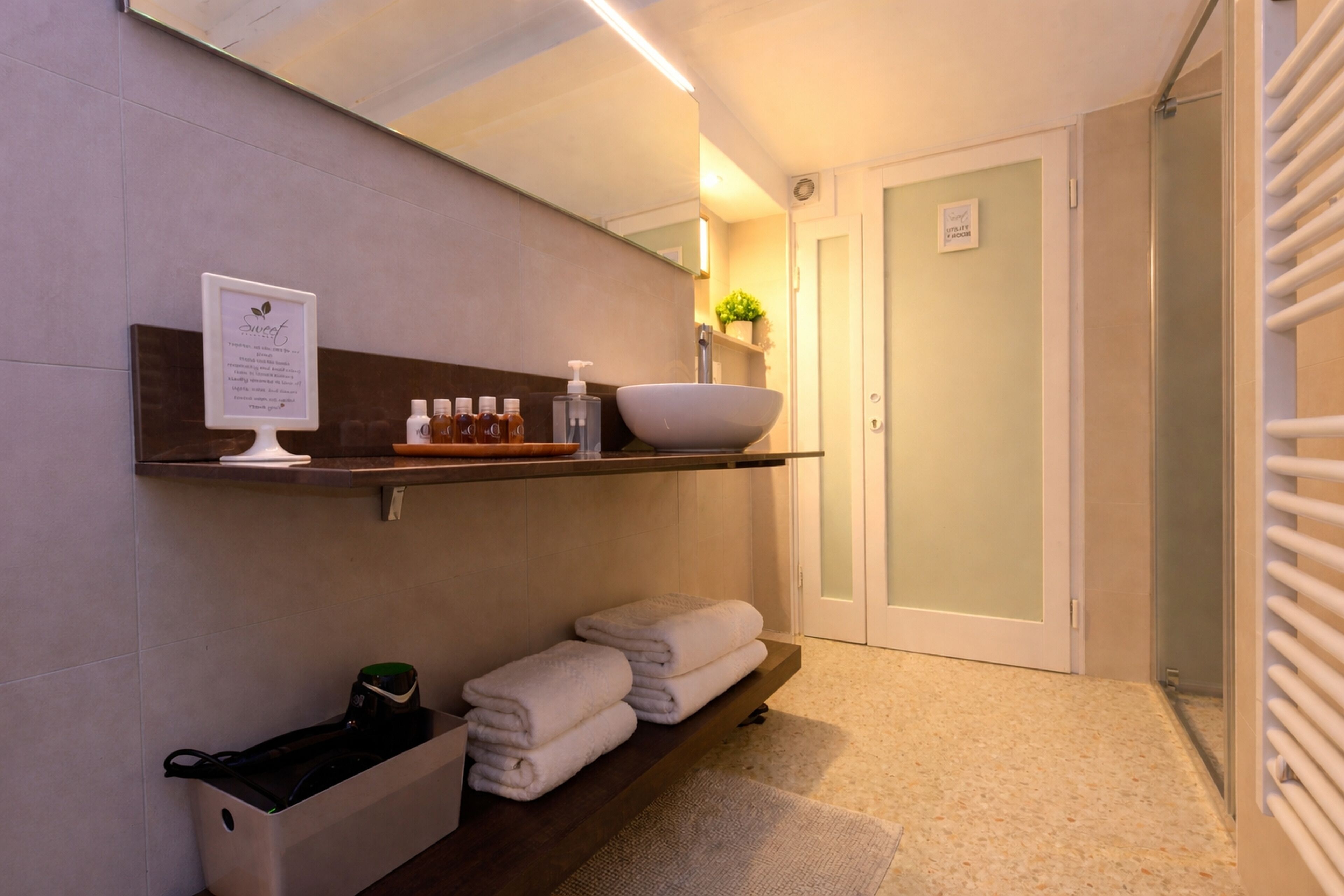 Une salle de bain avec un lavabo, un miroir, une étagère contenant des articles de toilette, des serviettes et une porte.