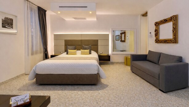 Une chambre d’hôtel moderne avec un grand lit, un canapé, une petite table et un miroir.