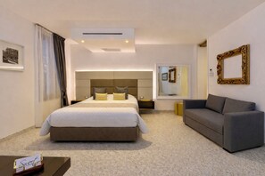 Une chambre d’hôtel moderne avec un grand lit, un canapé, une petite table et un miroir.
