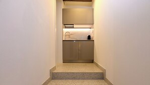 Un escalier étroit mène à une cuisine dotée d’un plan de travail en marbre et d’appareils électroménagers en acier inoxydable.