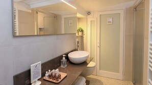 Une salle de bain moderne avec un grand miroir, un lavabo blanc et un espace douche.