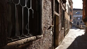 Une ruelle pavée étroite bordée de bâtiments historiques, dont l’un présente une grande fenêtre ornée de barreaux en métal.