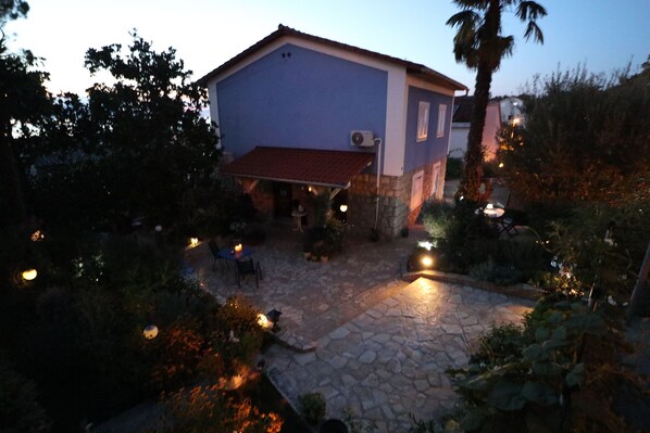 A house with a stone patio, a red awning, and outdoor lighting. - Apartment Njivice for 2 persons, 3 star "Lilis" apartment (Njivice)