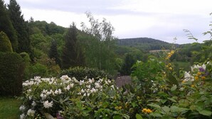 A garden with various flowers and trees, a building with a tiled roof, and a hilly landscape in the background. - Odenwald Lounge in the Bergstraße-Odenwald Nature Park (Reichelsheim (Odenwald))