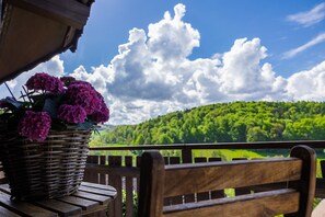 A wicker basket with purple flowers on a wooden bench with a view of a green hillside and a wooden railing.
