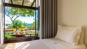 A hotel room with a bed, a window with curtains, and a view of a balcony with outdoor furniture and a tree.