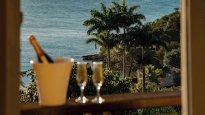 Ein Tisch mit einem Glas Champagner und einem Glas Wasser, mit Blick auf die Küste, Palmen und Berge.
