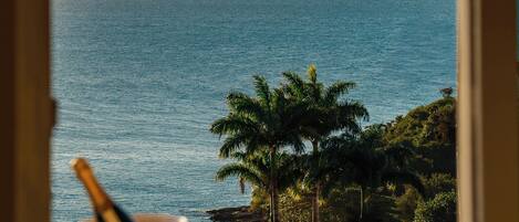 Una mesa con una copa de champán y una de agua, con vistas a la costa, palmeras y montañas.