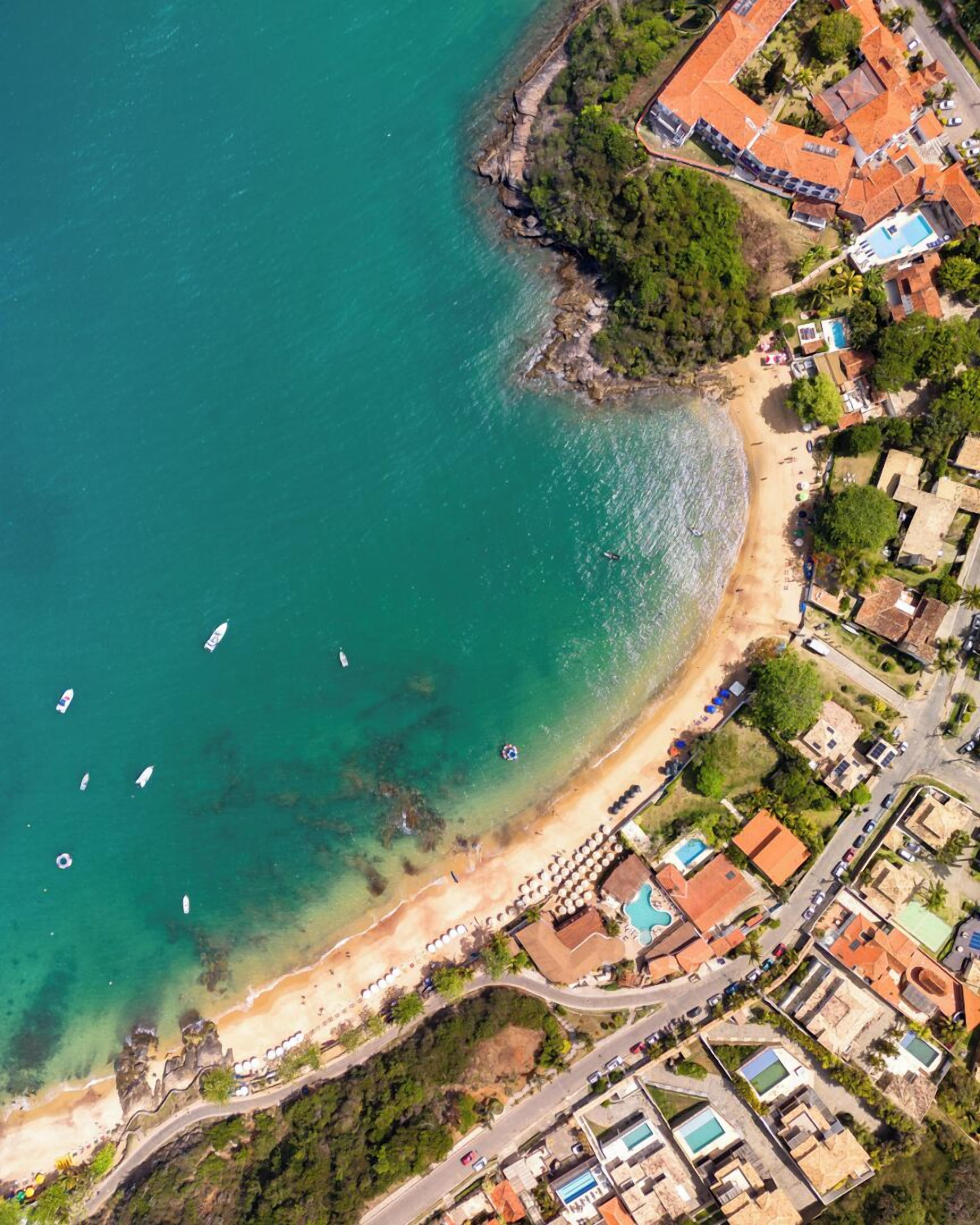 Vista aérea de una zona costera con playa, barcos y una área residencial con casas y piscina.