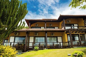 Un edificio de dos pisos con numerosas ventanas, un techo plano y un pequeño jardín con cactus y otras plantas.