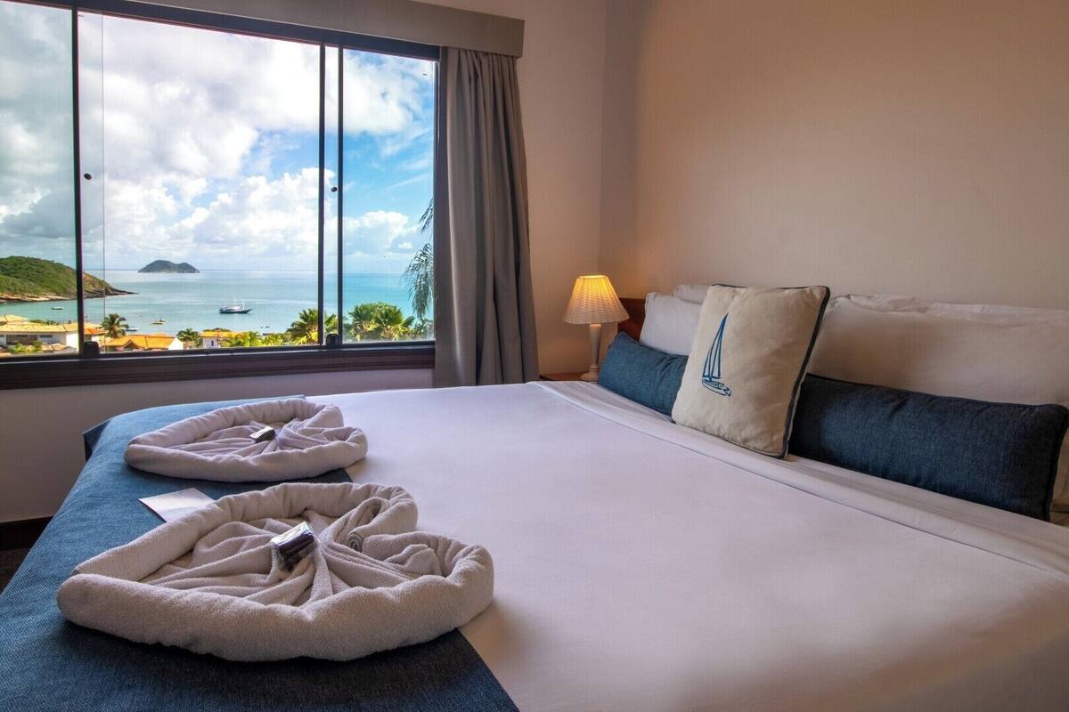 Una habitación de hotel con una cama grande, vista al mar y una lámpara en la mesita de noche.