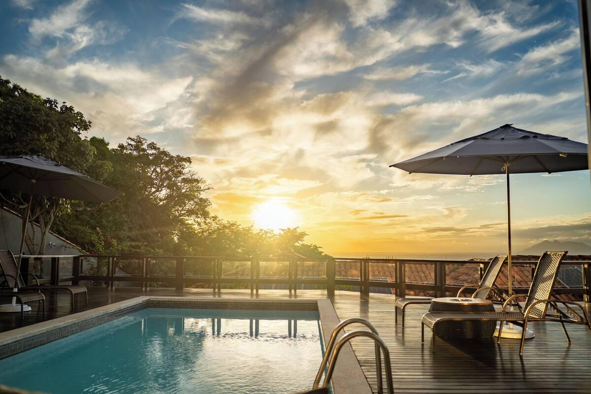 Zona de piscina con sillas de descanso y sombrillas, con vistas a un paisaje idílico.