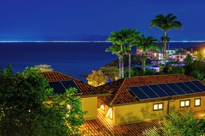 A coastal property with solar panels on the roof, palm trees, and a view of the ocean at night. - Búzios Mar Hotel (Búzios)
