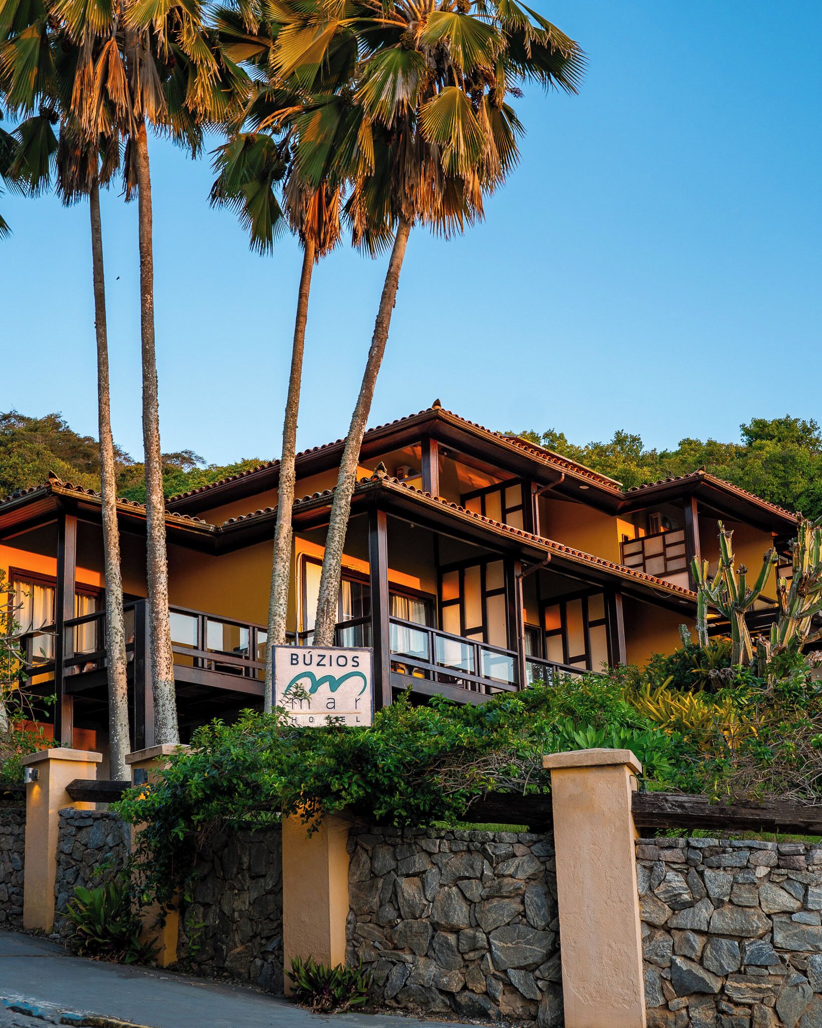 Un hotel con un letrero que dice "Búzios Mar Hotel". Presenta un estilo arquitectónico tradicional con un balcón y muros de piedra.