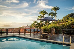 A pool area with lounge chairs and an umbrella, surrounded by palm trees and a view of the ocean. - Búzios Mar Hotel (Búzios)