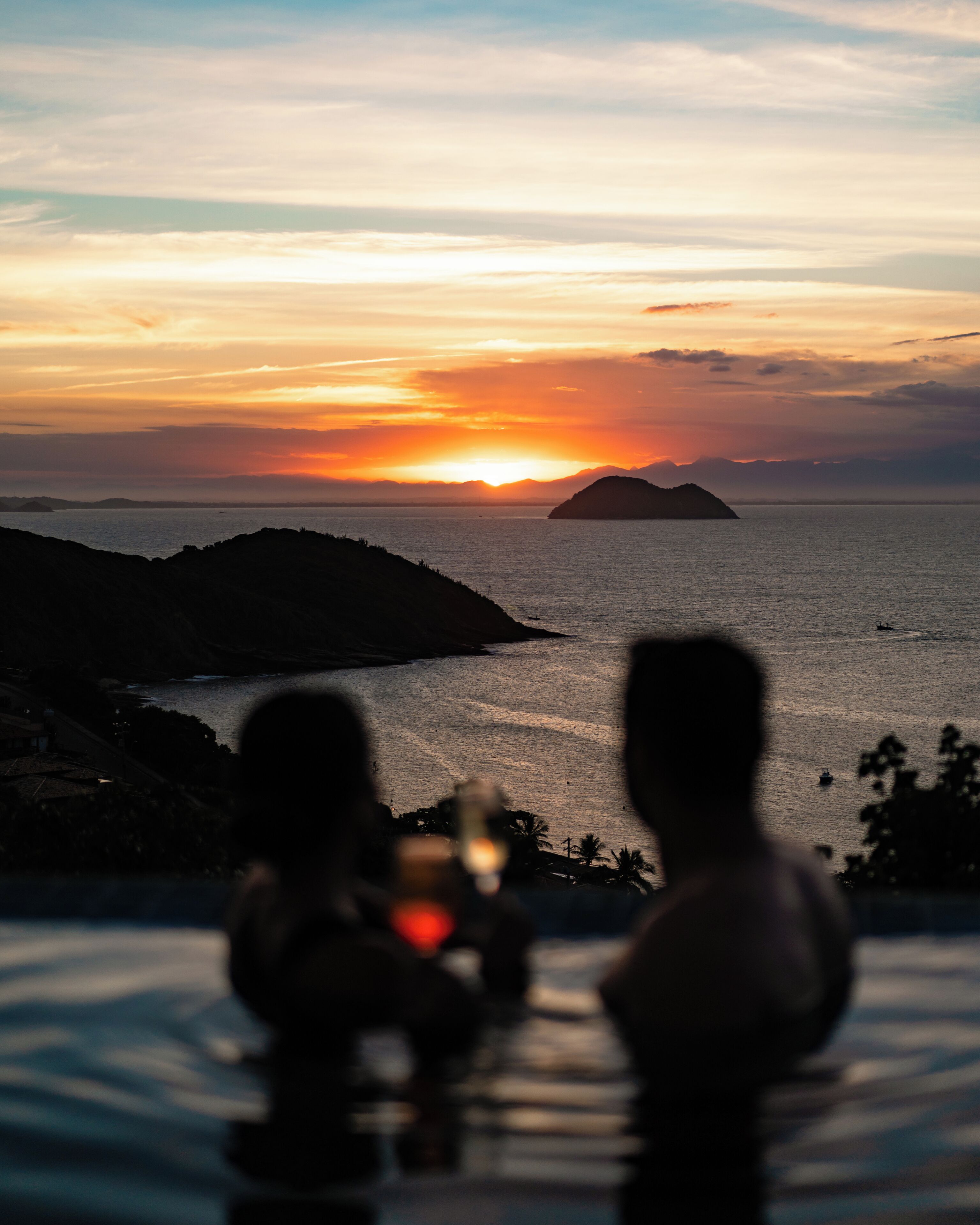 A sunset view from an infinity pool overlooking a body of water with distant landforms.
