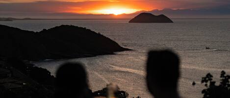 A sunset view from an infinity pool overlooking a body of water with distant landforms.