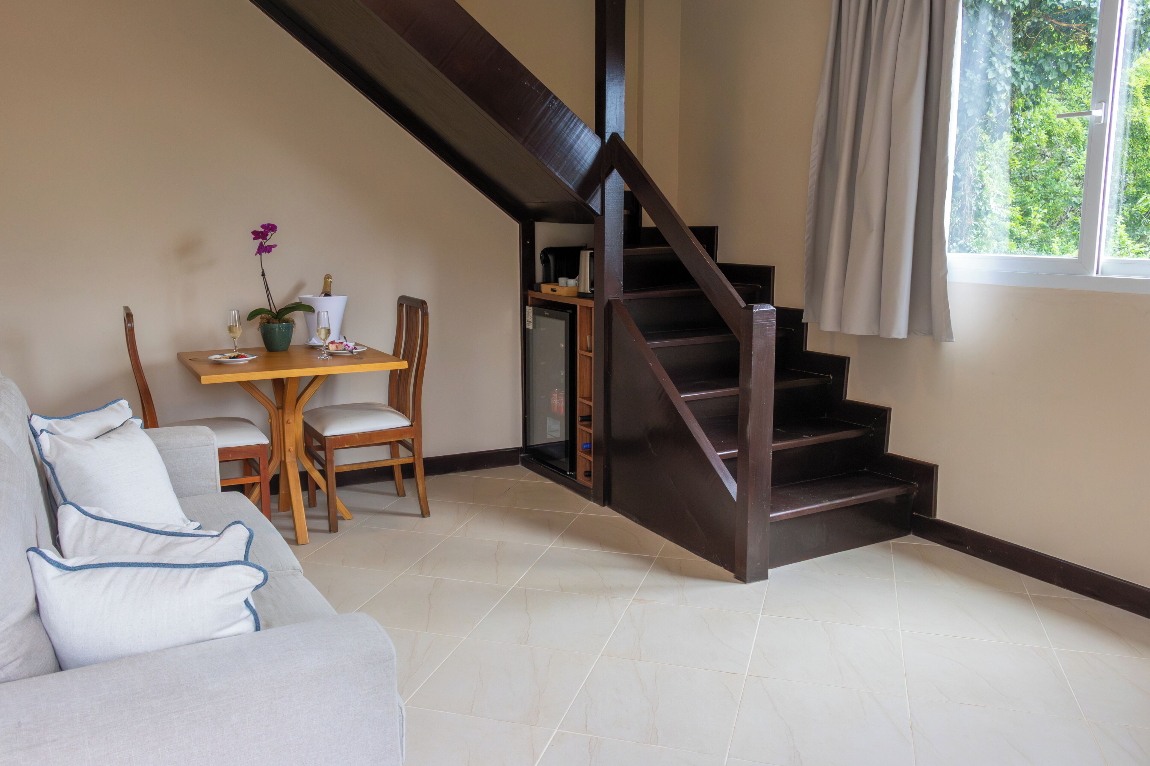Un salon avec un escalier, un coin repas avec des chaises et une table, et une fenêtre avec des rideaux.