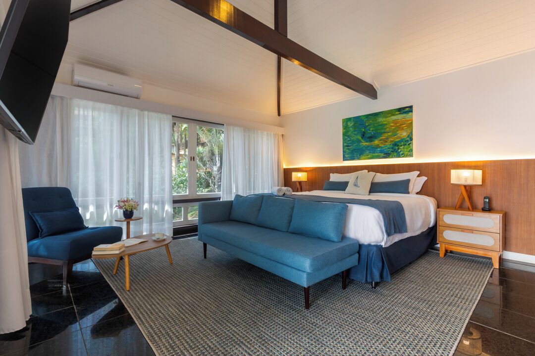 A modern hotel room with a large bed, a blue sofa, a small table, and a TV.