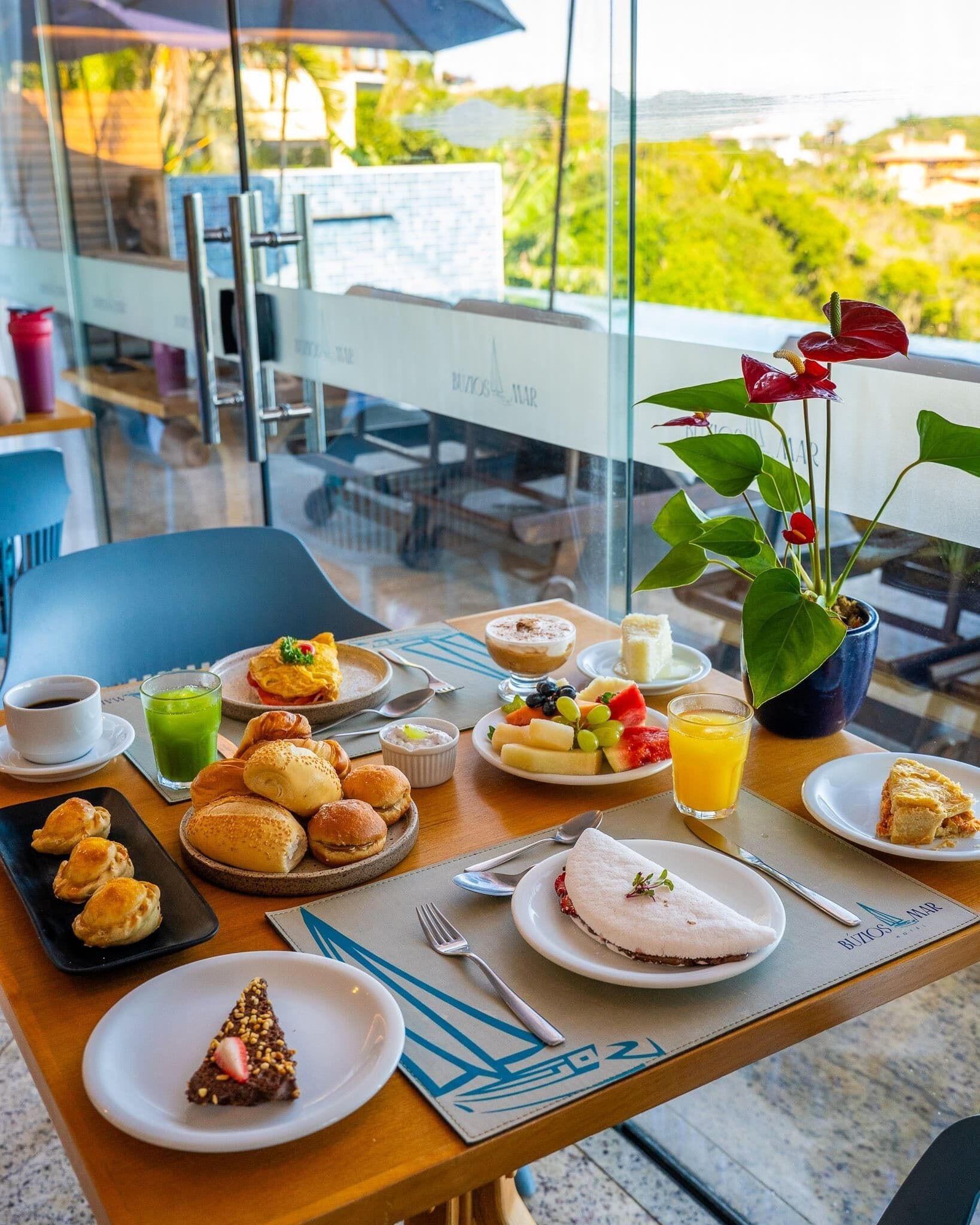 A breakfast table with various dishes, a plant, and a view of greenery outside.