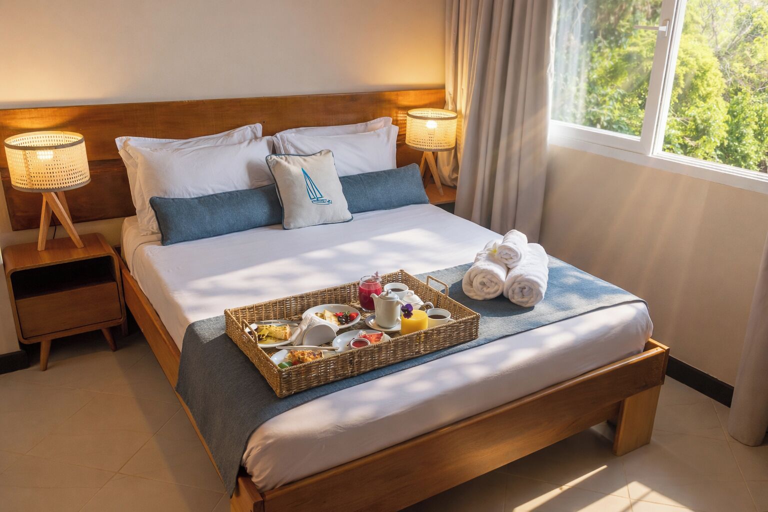 A neatly made bed with a tray of breakfast items, two bedside lamps, and a window with curtains.