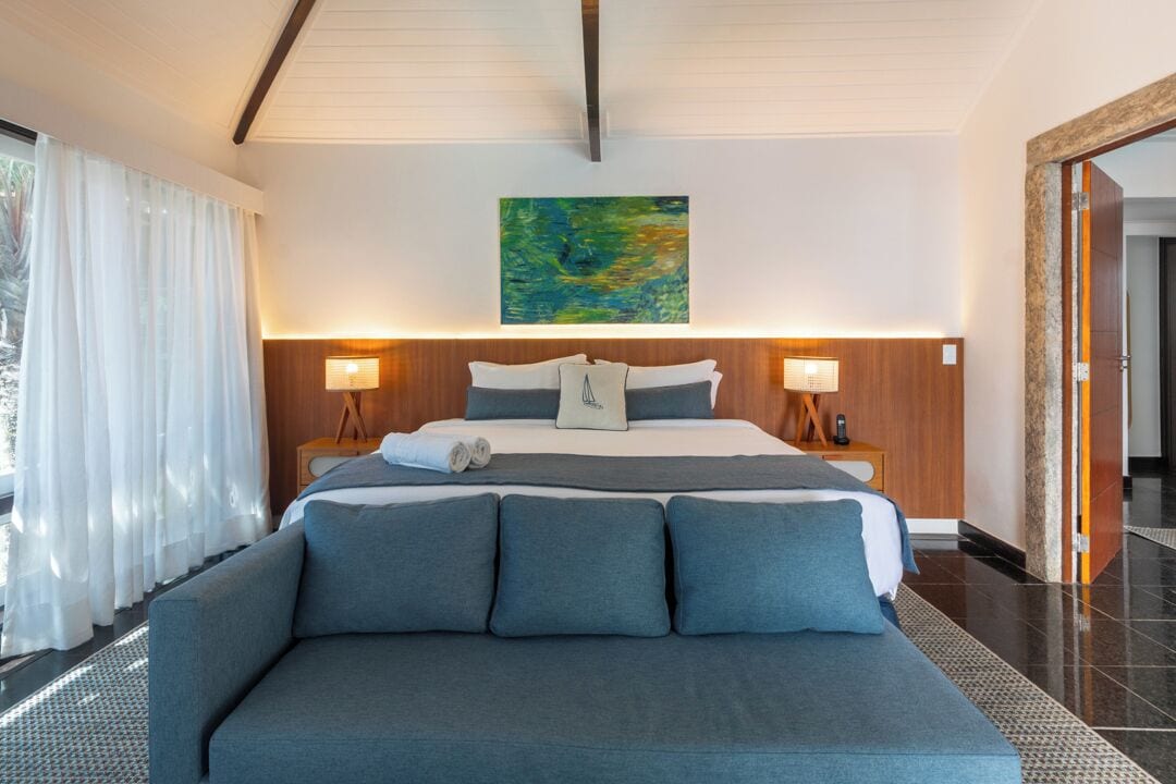 Ein modernes Hotelzimmer mit einem großen Bett, zwei Nachttischen mit Lampen, einem großen Fenster mit Vorhängen und einem Bild an der Wand.
