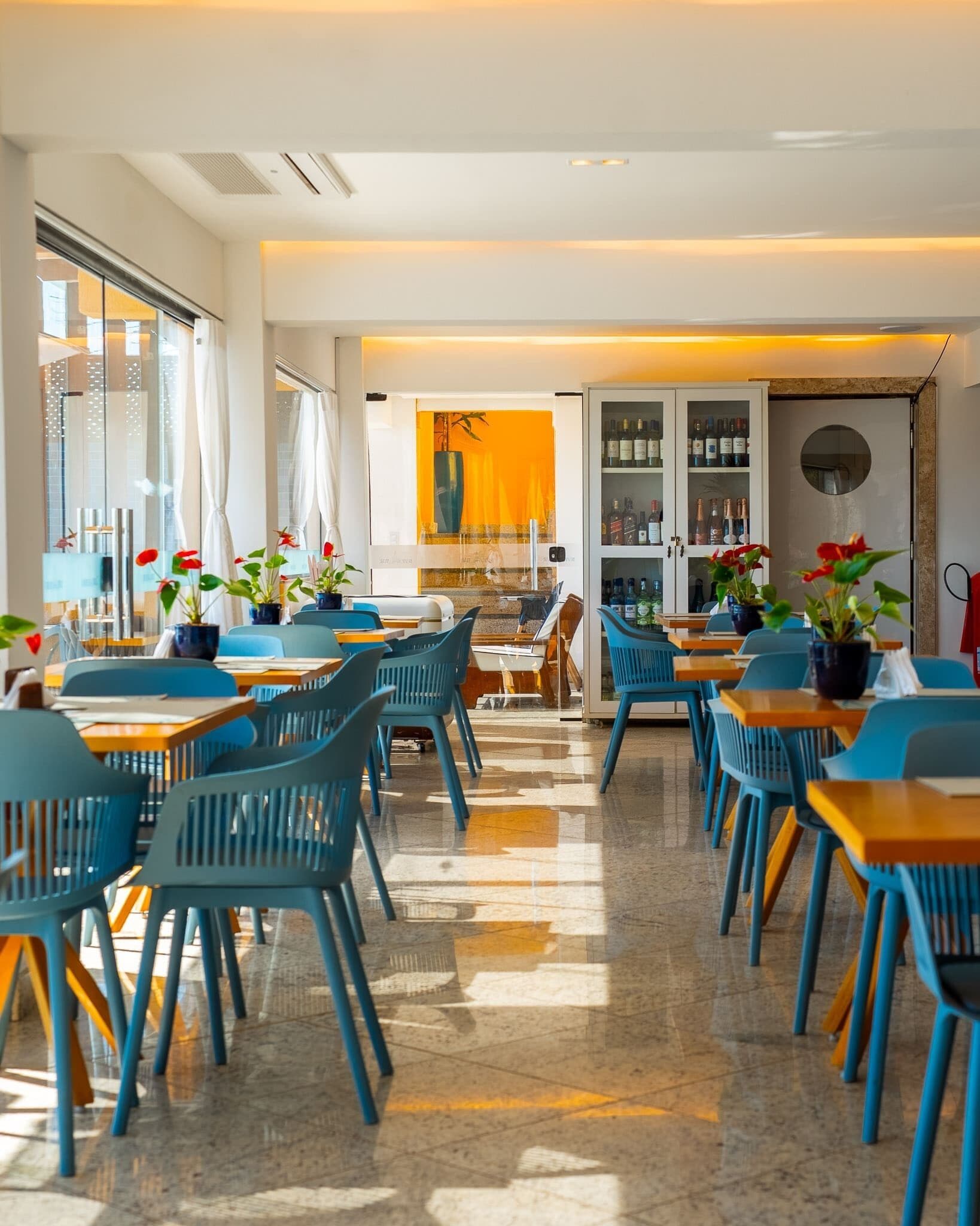 A modern dining area with blue chairs and tables, a glass partition with a view, and a bar area with bottles.