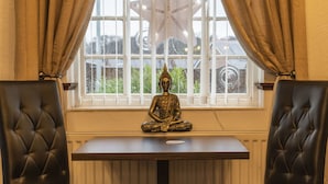 A room with a window, a Buddha statue on a table, and two leather chairs.