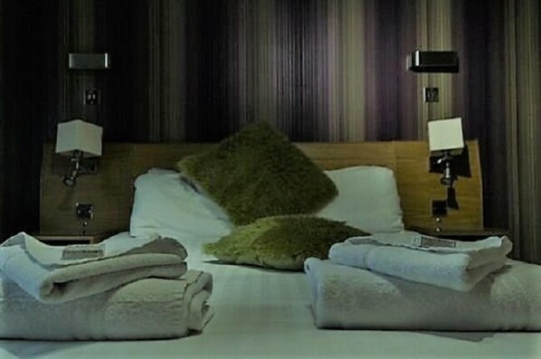 A hotel room with a wooden headboard, two bedside lamps, a green pillow, and neatly folded towels on the bed.