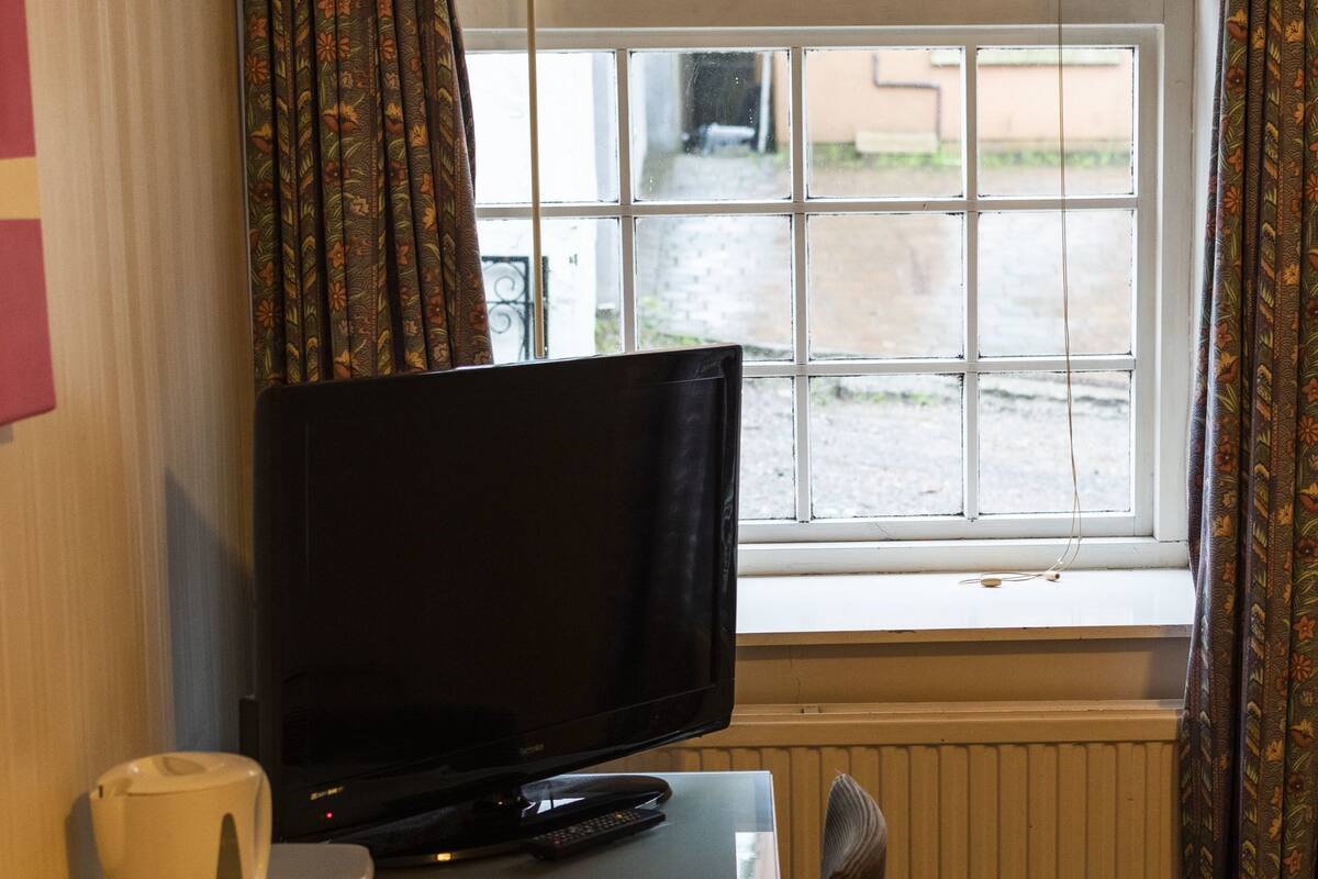 A room with a television on a table, a window with curtains, and a radiator.