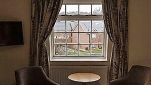 A hotel room with a bed, two armchairs, a small round table, and a window with curtains.