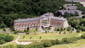 A large, multi-story hotel with a central courtyard, surrounded by lush greenery and a golf course.