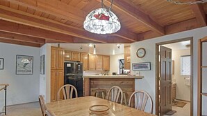 Un coin repas avec une table et des chaises en bois, un lustre, des meubles de rangement en bois et, au fond, une cuisine.